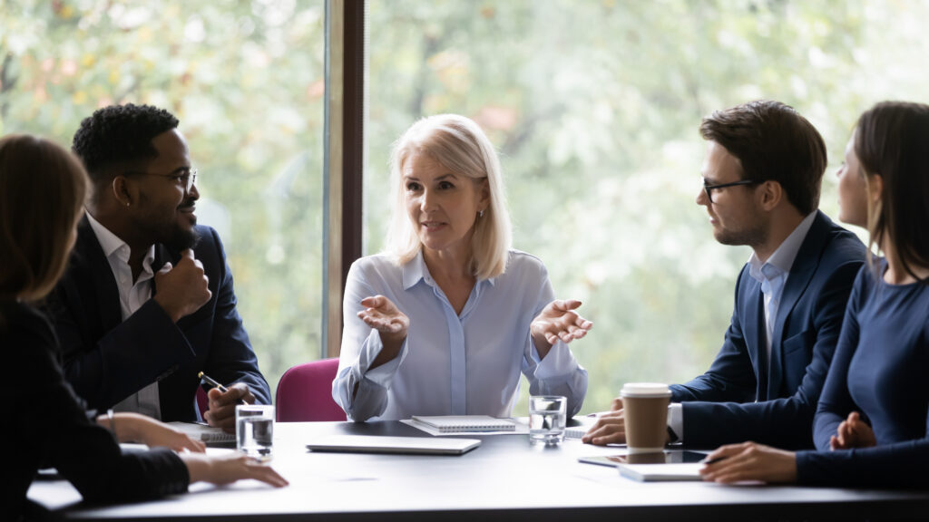 People sitting around a table. One person is at the head and appears to be the leader.